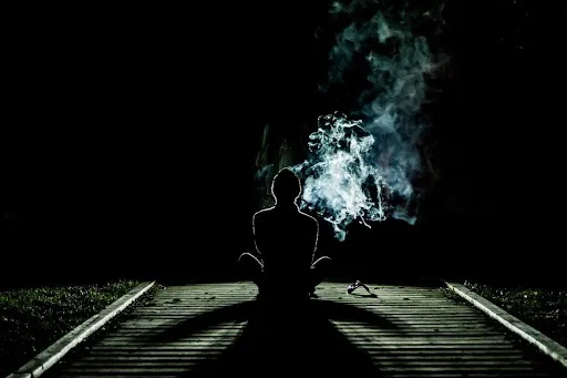 Dark silhouette of man smoking outdoors at night 
